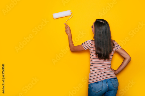 Cute young woman with paint roller while working during renovation of apartment