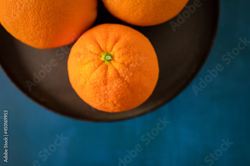 A bowl or platter of vibrant navel oranges on a bright blue textured background photo