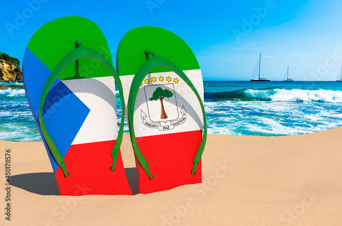 Flip flops with Equatoguinean flag on the beach. Equatorial Guinea resorts, vacation, tours, travel packages concept. 3D rendering