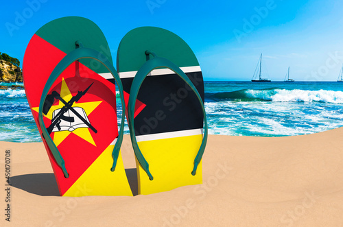 Flip flops with Mozambican flag on the beach. Mozambique resorts, vacation, tours, travel packages concept. 3D rendering
