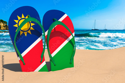 Flip flops with Namibian flag on the beach. Namibia resorts, vacation, tours, travel packages concept. 3D rendering
