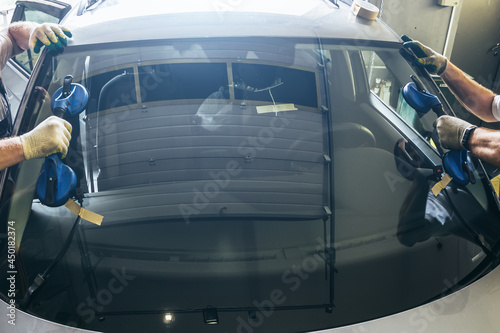 Φωτογραφία Mechanic workers hands changes broken windscreen on new windshield on car in service station close up