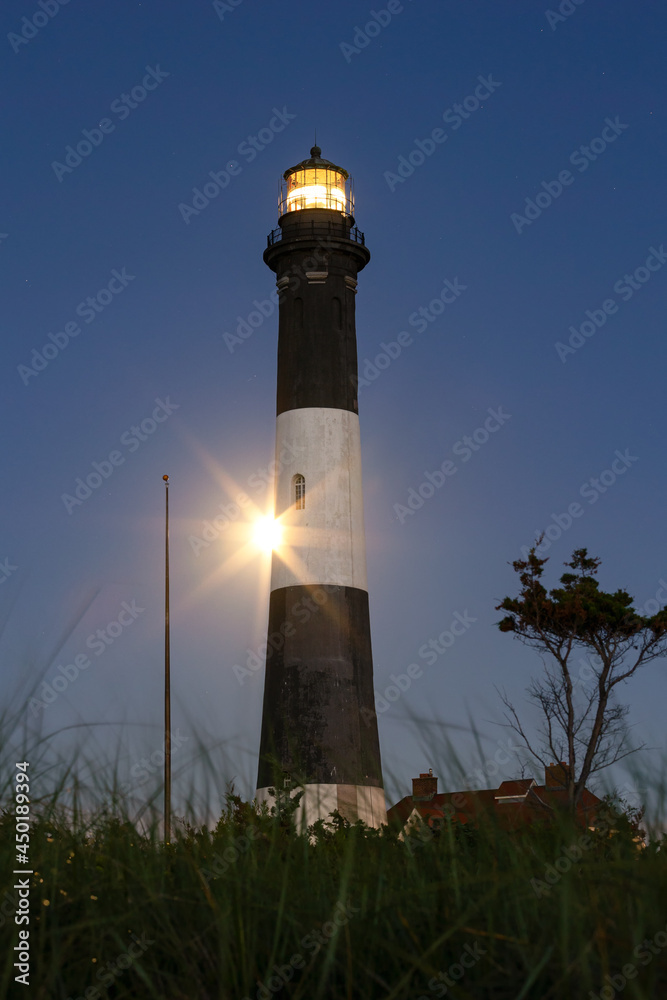 Full moon rising behind a tall stone lighthouse. Fire Island, New York