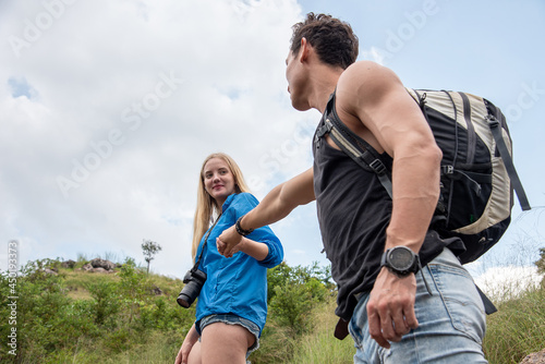 woman carrying a camera, holding a man is hand carrying a suitcase up the mountain