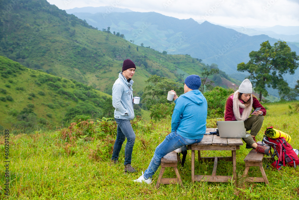 Group of Asian people friends with backpack enjoy outdoor lifestyle activity in nature hiking and camping together on the mountain. Man and woman friendship sit on outdoor chair and drink hot coffee 