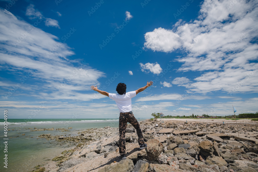 Happy asian man standing on the rock beach with blue sky Happy asian man standing on the rock beach with blue sky