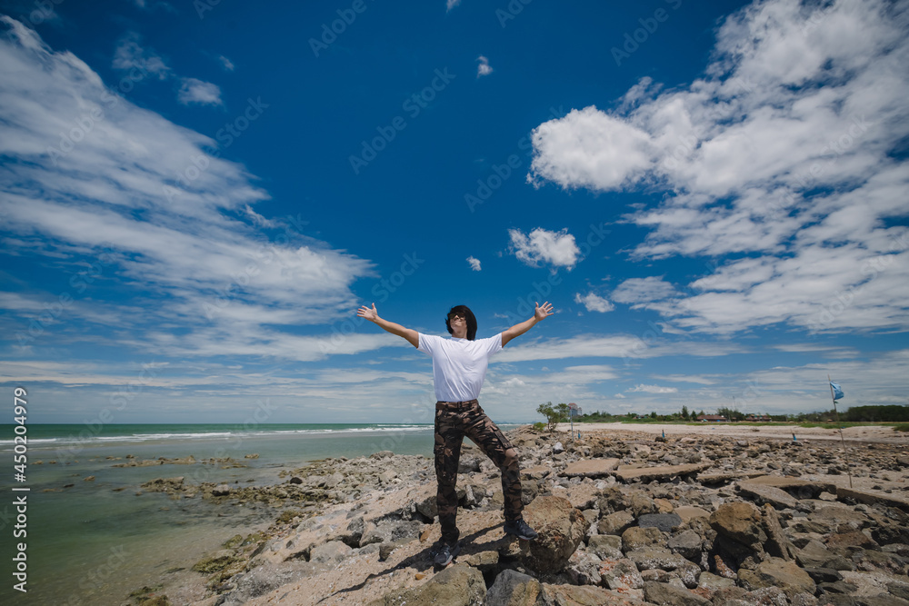 Happy asian man standing on the rock beach with blue sky Happy asian man standing on the rock beach with blue sky
