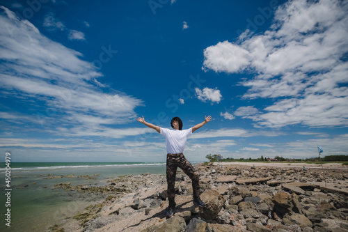 Happy asian man standing on the rock beach with blue sky