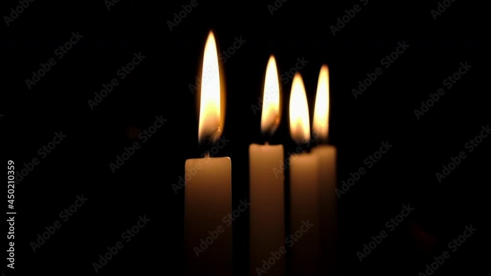 Flames of four candles flicker in darkened room
