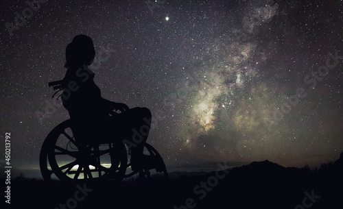 Silhouette Disabled handicapped woman is sitting on wheelchair looking Night landscape with colorful Milky Way