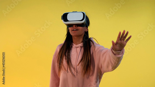 Multiracial girl using virtual reality glasses while standing against yellow background. © art24pro