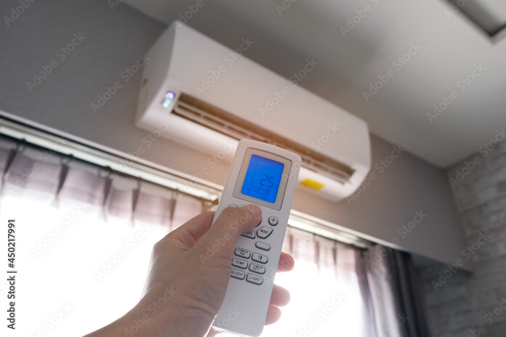 Man's hand using remote control open The air conditioner is cooled to 25 degrees Celsius in his bedroom. Health concepts and energy savings Man's hand using remote control open The air conditioner is cooled to 25 degrees Celsius in his bedroom. Health concepts and energy savings