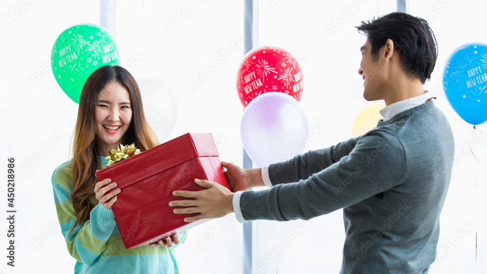 Two Asian lovers enjoying gift exchange together with happy faces at romantic indoor party decorated by fancy balloon to celebrate ecstatic love in winter. Two Asian lovers enjoying gift exchange together with happy faces at romantic indoor party decorated by fancy balloon to celebrate ecstatic love in winter.