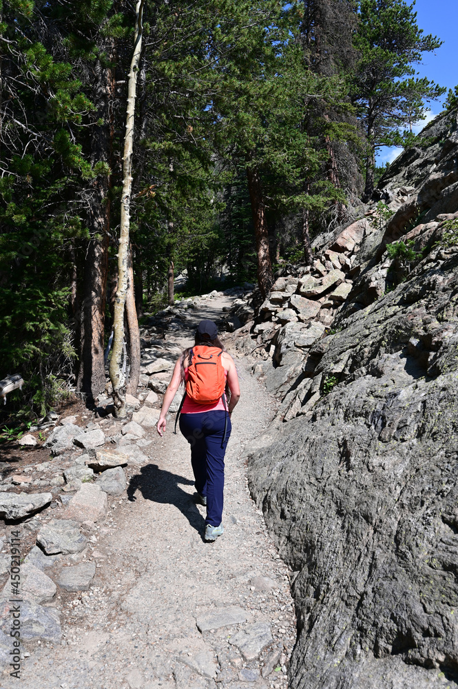 Young woman hiking Emerald Lake Trail in Rocky Mountain National Park, Colorado on sunny summer morning.