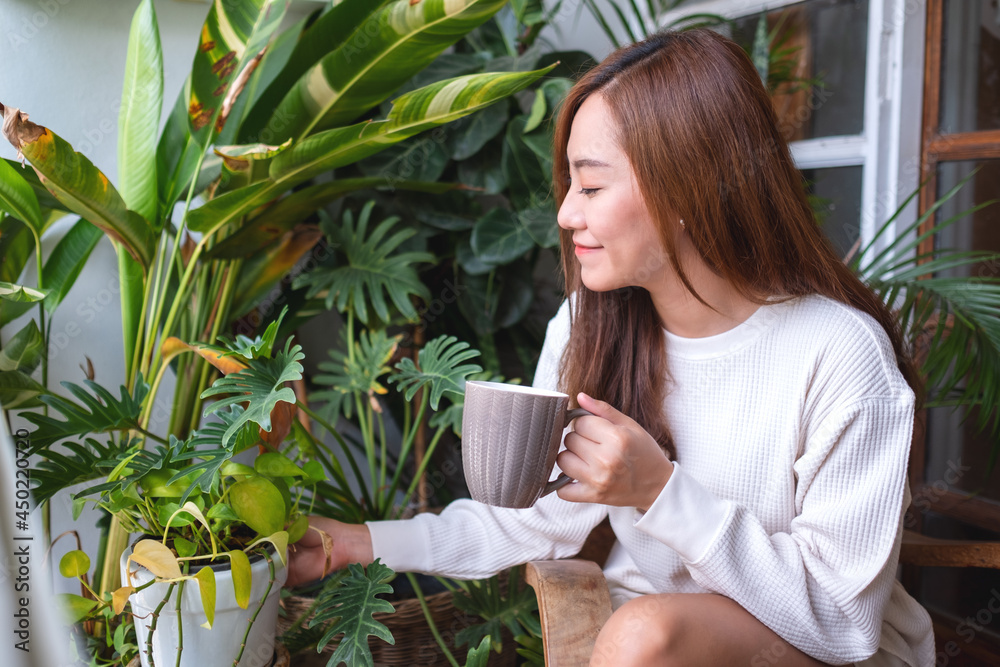 Portrait image of a beautiful asian woman drinking hot coffee and taking care of houseplants garden on balcony at home Portrait image of a beautiful asian woman drinking hot coffee and taking care of houseplants garden on balcony at home
