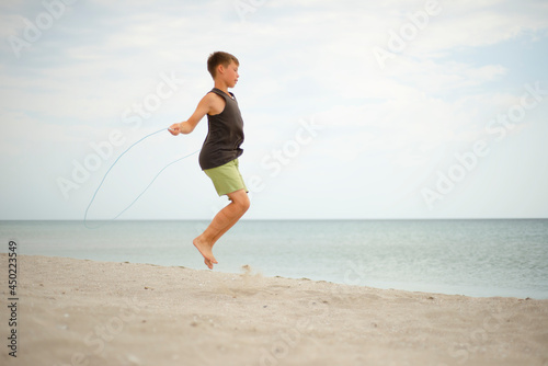 The boy on the beach is jumping rope. Lifestyle themes. Healthy lifestyle themes. Sports and training. © LKoroleva