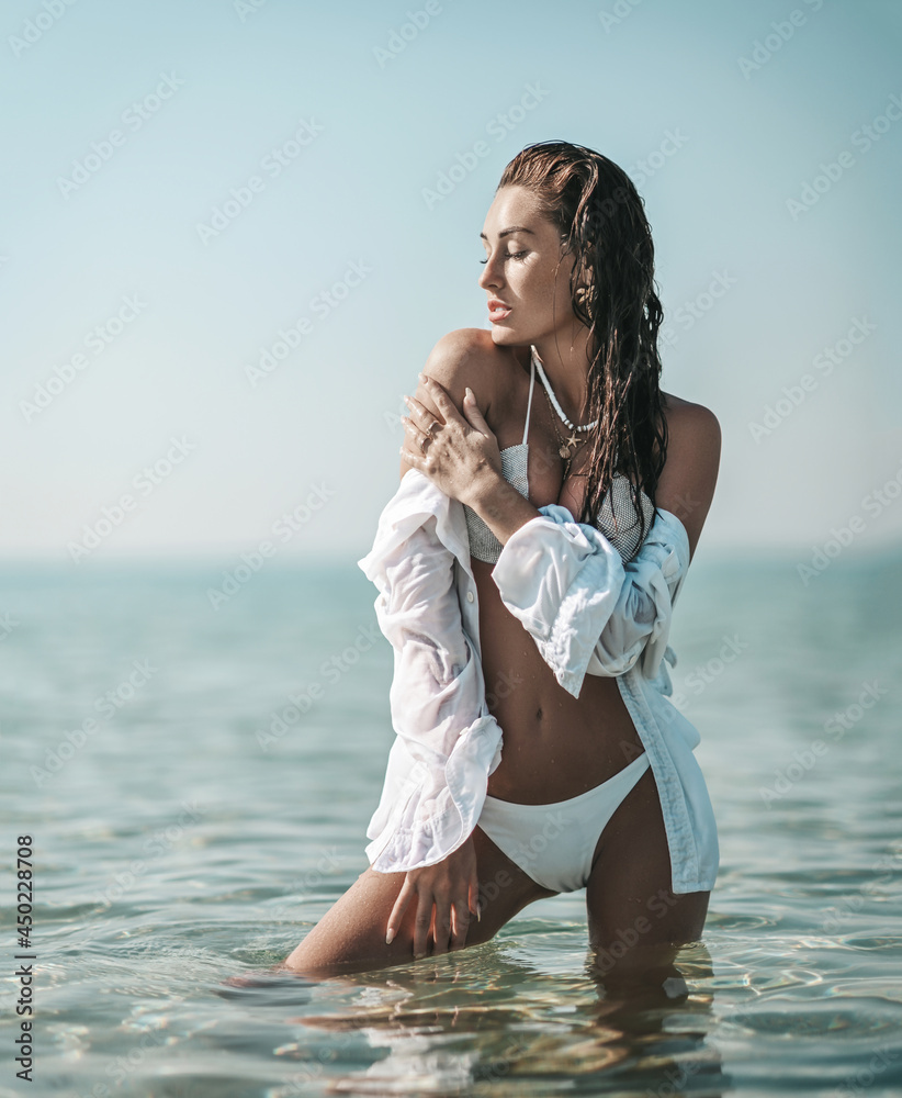 Sexy young slim woman girl in white bikini and shirt stands in waist-deep  sea, facing sun, touching tanned shoulder, feeling pleasure during  vacation. Summer vibes. On the beach Stock Photo | Adobe