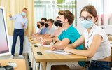 Diligent teenage girl in protective face mask studying in college with classmates. New life reality in coronavirus pandemic