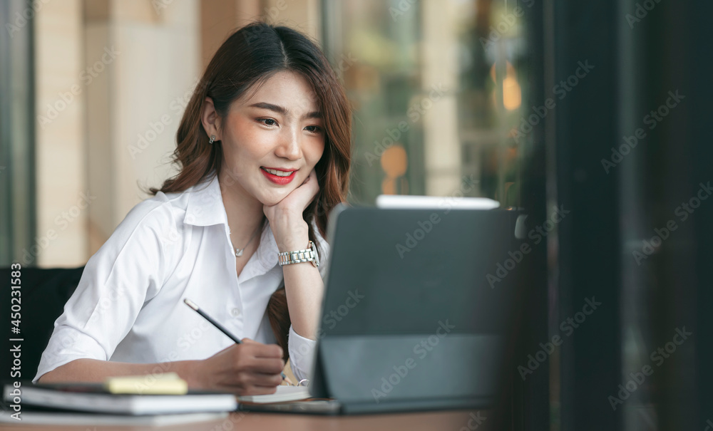 Beautiful asian woman writing note and working on tablet computer with happiness while sitting at her desk office. Beautiful asian woman writing note and working on tablet computer with happiness while sitting at her desk office.