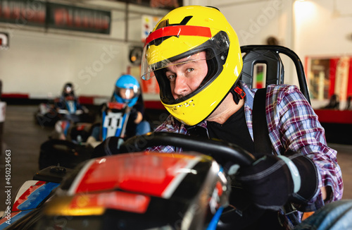 Glad smiling male in helmet and other people driving cars for karting in sport club indoor