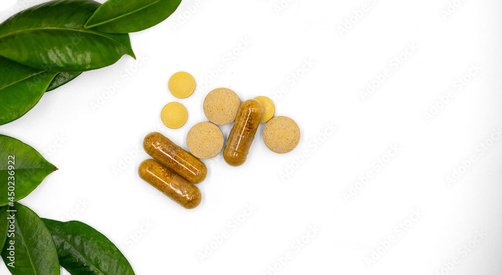 Herbal pills and capsule with leaves from fresh green source herbs in a display set against a white background. Herbal pills and capsule with leaves from fresh green source herbs in a display set against a white background.