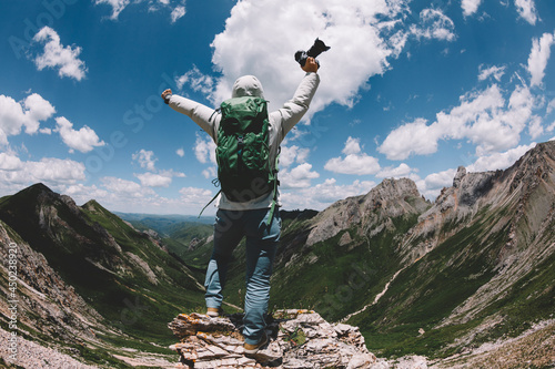 Cheering woman photographer with camera on high altitude mountain top