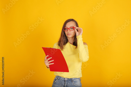 a young beautiful blonde girl in a yellow jacket and jeans holds a red folder in her hands