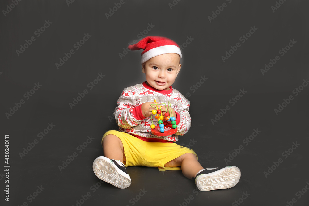 a little boy in a Christmas sweatshirt and a Santa Claus hat with a toy in his hands a little boy in a Christmas sweatshirt and a Santa Claus hat with a toy in his hands