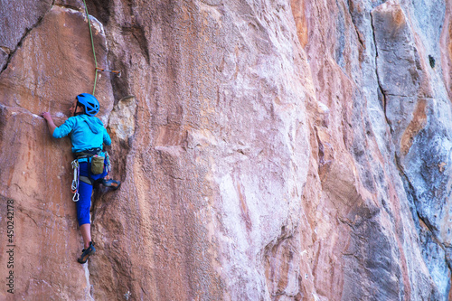 A woman in a helmet climbs a beautiful blue rock.