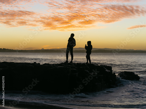 Silhouette of Friends Taking Picture at Sunset Time in a Rock Close to the Ocean.Friends Concept
