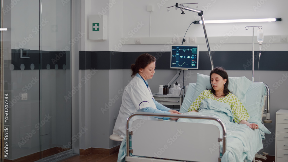 Obraz premium Specialist doctor putting oximeter checking pulse talking with sick woman explaining sickness symptom during recovery appointment. Patient resting in bed waiting for disease treatment in hospital ward