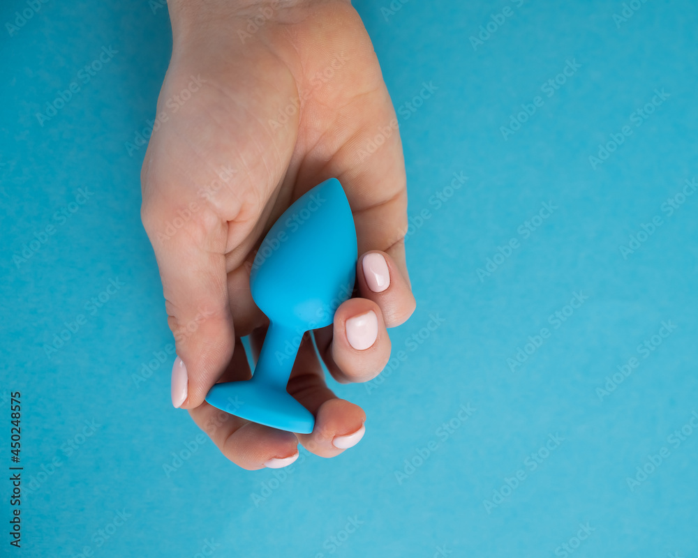 A woman is holding a blue anal plug on a blue background