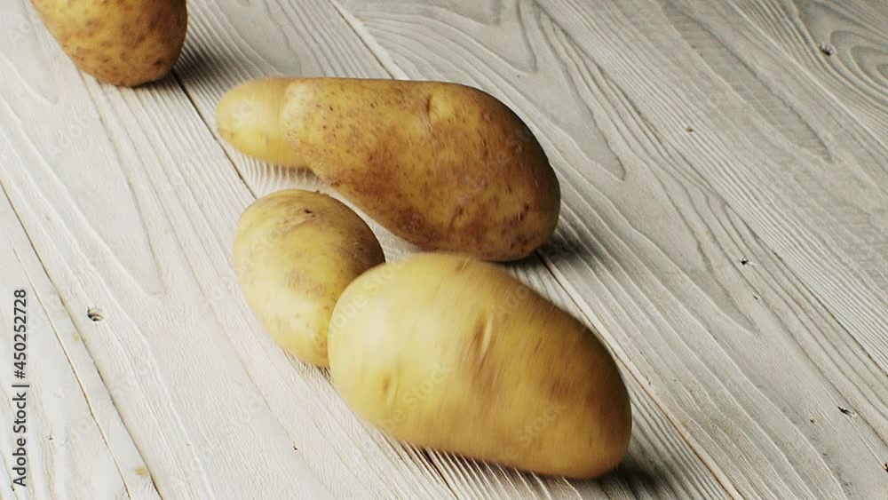 A raw potato with a peel rolls on a wooden table A raw potato with a peel rolls on a wooden table