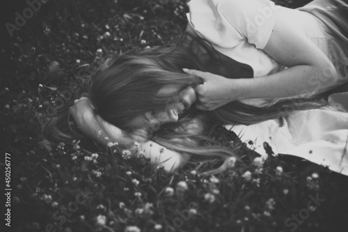 Happy girl with long hair in a dress lies and sleeps in the grass with white clover flowers on a warm summer evening. Black and white photo of beautiful sleeping woman in the field with wildflowers