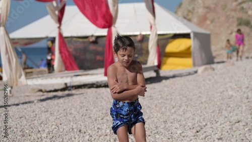 wet little boy in blue shorts freeze and shiver shake on summer beach after swimming during holiday vacation travel to sea