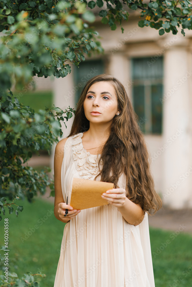 Naklejka premium A romantic young woman in a summer dress holds a vintage letter in her hands