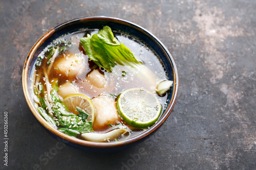 Oriental soup. Vegetable and meat broth with fresh herbs, sesame, lime and dumplings in an oriental bowl, on black stony background, top view with a copy space. An Eastern delicacy.