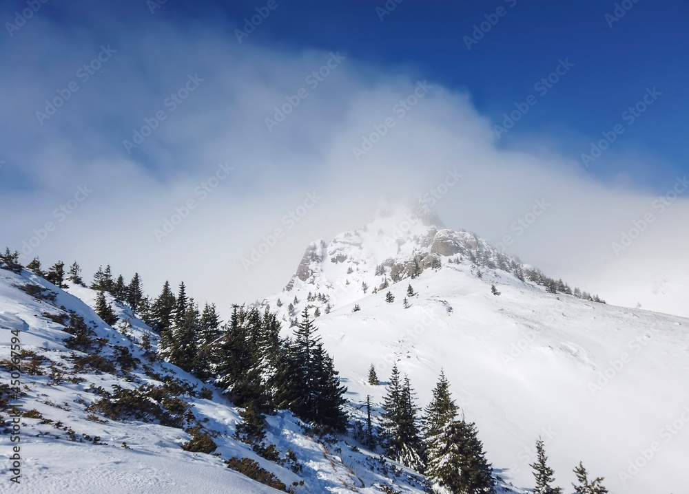 Snow covered rock formations under gusty freezing wind , high up in the Ciucas mountains in Romania , part of the Carpathian range in eastern Europe , wintertime landscape.