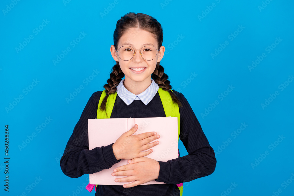 Photo of good mood cheerful smiling clever girl hug embrace book wear backpack isolated on blue color background Photo of good mood cheerful smiling clever girl hug embrace book wear backpack isolated on blue color background