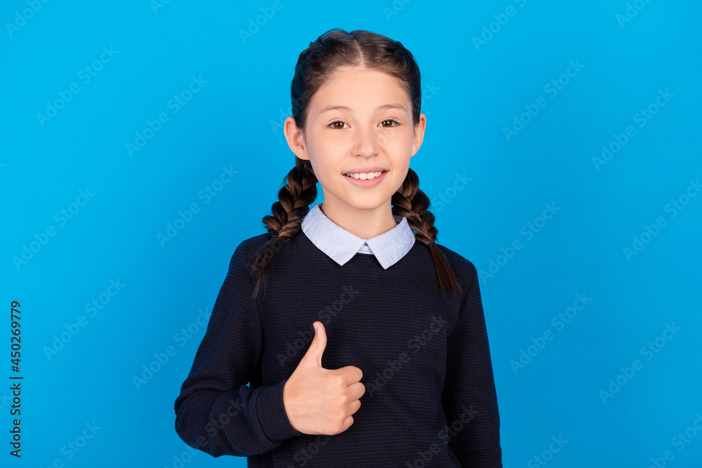 Photo of happy good mood smiling schoolgirl showing thumb up recommend isolated on blue color background Photo of happy good mood smiling schoolgirl showing thumb up recommend isolated on blue color background