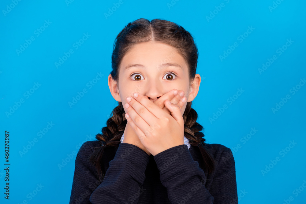 Photo of young mute speechless little girl hold hands cover mouth secret isolated on blue color background Photo of young mute speechless little girl hold hands cover mouth secret isolated on blue color background