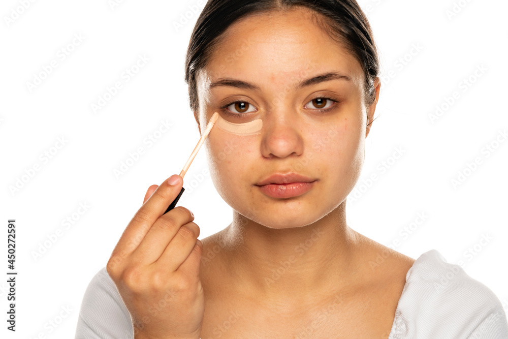 closeup of a young beautiful woman applies concealer under her eye closeup of a young beautiful woman applies concealer under her eye