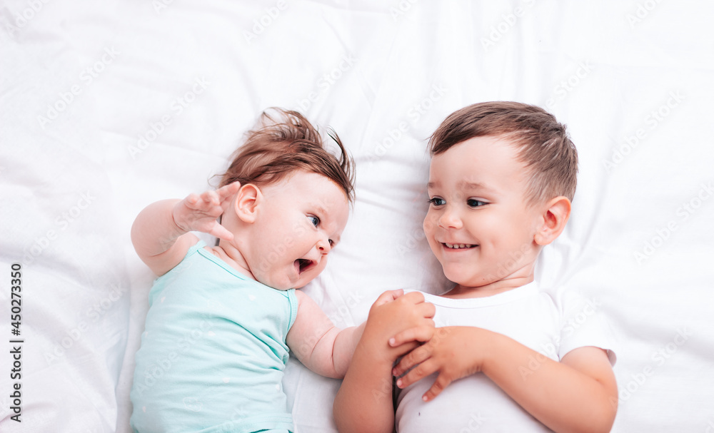 happy little brother hugs his little sister lying on a white blanket happy little brother hugs his little sister lying on a white blanket