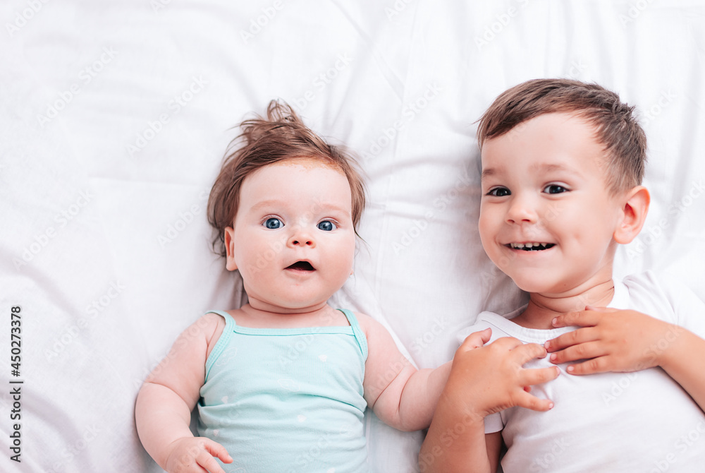 happy little brother hugs his little sister lying on a white blanket happy little brother hugs his little sister lying on a white blanket