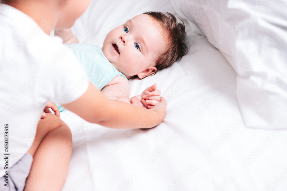 The older brother lovingly hugs his newborn sister and holds her hand as they lie together in bed. The older brother lovingly hugs his newborn sister and holds her hand as they lie together in bed.