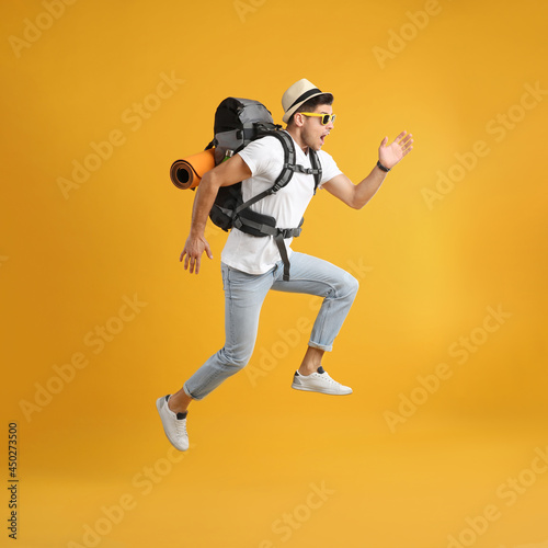 Emotional male tourist with travel backpack jumping on yellow background