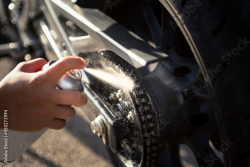 Detail of the hand of a biker woman cleaning and oiling the chain of the motorcycle. Motorcycle care and maintenance concept.