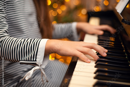 Girl's hands on the piano, close-up, beautiful bokeh in the background, woman playing the piano. Christmas lights and music, concert, family time, holidays concept.