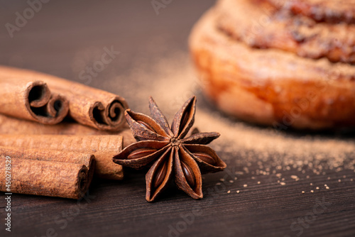 Close-up shot of cinnamon sticks and anise star with a bun on the background. Cooking spicy bread with cinnamon