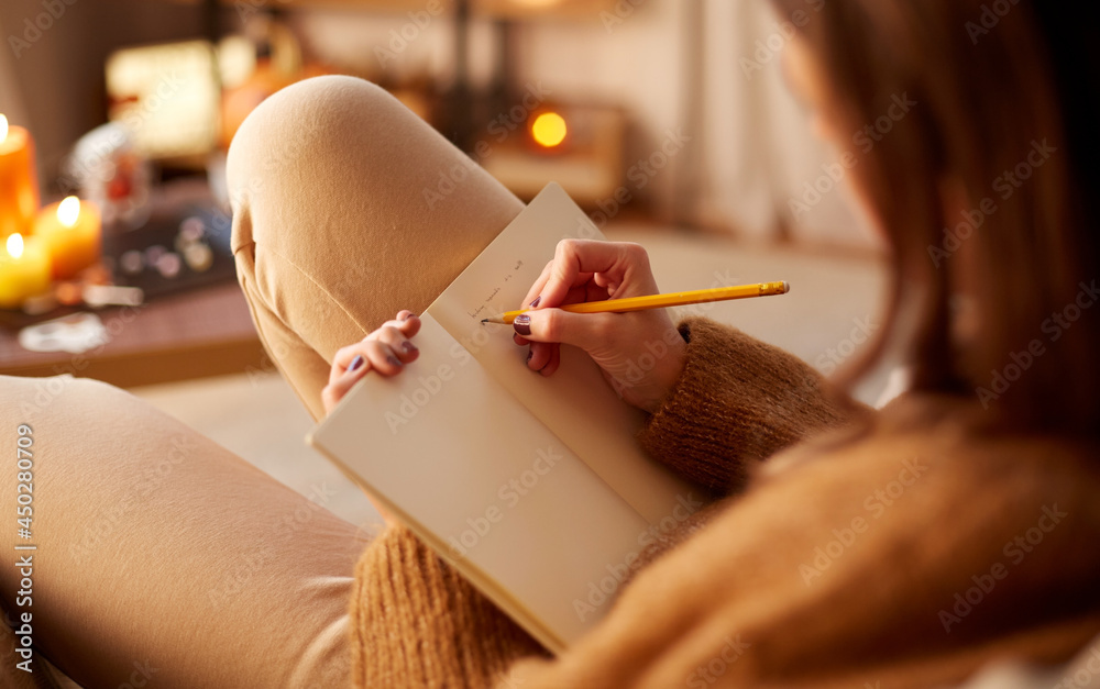 halloween, holidays and leisure concept - close up of young woman with pencil writing to diary and resting her feet on table at cozy home - obrazy, fototapety, plakaty 